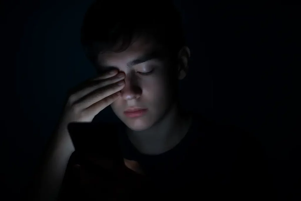 adolescente no celular coçando o olho